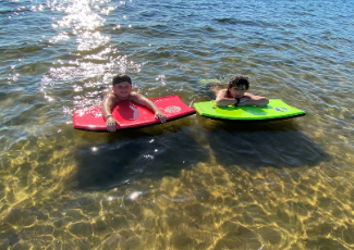 two young boys laying on swim boards in the lake